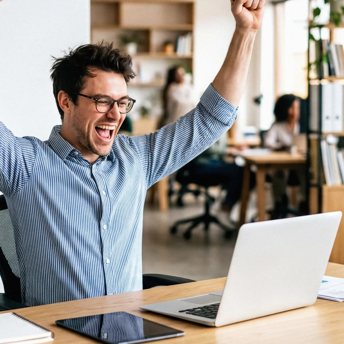 An officer at a laptop punching a fist in the air in a bright open-plan office